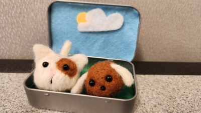 A decorated open Altoid tin with a needle felted cat and dog sitting in it. 