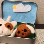 A decorated open Altoid tin with a needle felted cat and dog sitting in it. 
