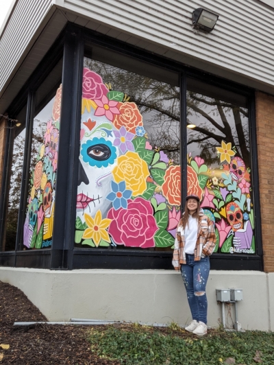 Artist standing in front of her colorful window mural