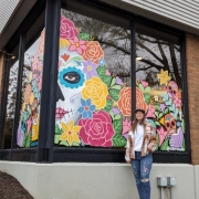 Artist standing in front of her colorful window mural
