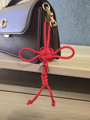 Red string tied into clover-like knot attached to a purse as a bag decoration 