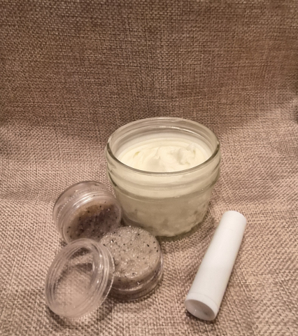 various skin care items display against a burlap background, including: mason jar of lotion, white chapstick tube, and two clear containers or coffee sugar scrub (one opened)