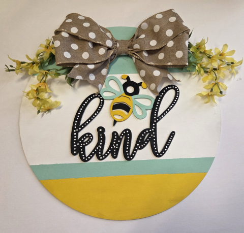 round wooden wreath with a Bee and the word kind with a bow and yellow flowers at the top